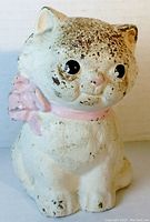 Front view of the white cast iron kitten bank with worn and chipped paint, pink collar visible