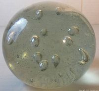 View of clear glass paperweight showing dispersed bubbles inside and the internal hazy cloud formation.