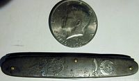 Photo showing the front side of the pocket cutting utensil with the Shriners emblem embossed on the metal handle beneath a coin for scale.