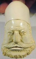 Close-up view of the carved man's head showing detailed beard, mustache, facial features, and tall hat with tassel.