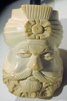 Close-up front view of carved man's head showing detailed facial features and turban badge