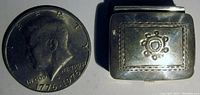 Photo showing pill box next to 1976 US quarter for size comparison, depicting detailed hand-tooled patterns and rounded rectangular shape.