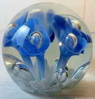 Photo showing front view of clear glass paperweight with 5 blue trumpet flower inclusions and clear bubbles inside.