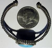 Top view of silver twisted wire design cuff bracelet with large turquoise stone compared to a coin for scale.