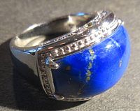 Close-up image showing large polished blue lapis lazuli with gold flecks set in detailed sterling silver ring band.