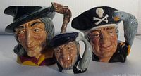 Front view of the three Royal Doulton figural mugs showing Pied Piper, Captain Ahab, and Long John Silver, highlighting detailed paint and character design.