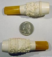 Top and bottom view of two meerschaum cigar holders with amber stems placed alongside a quarter for scale.