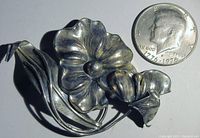 Close-up image of the vintage sterling pansy flower pin with a half dollar coin for size comparison, showing intricate textured petals, leaf and buds.