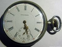 Front view of Waltham pocket watch face showing white dial with Roman numerals and subsidiary seconds dial, ornate gold hands, and winding crown.