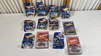 12 Hot Wheels cars in blister packs arranged on a white surface, packaging shows wear and water damage.