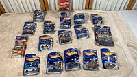 17 Hot Wheels toy cars laid out on a table, all in original blister card packaging with visible water damage and tearing