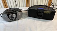 Two radios shown side by side on a white surface: left is a compact Insignia CD player and radio, right is a larger black HPS IP 550 radio.