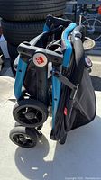 Folded Q-Bit stroller showing four double wheels, folded handlebar with blue accents, black fabric seat section.
