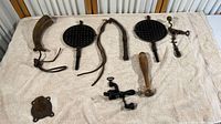 Full display of vintage western collection items including two cast iron waffle irons, powder horn, hand drill and other parts.