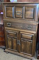 Front view of the wooden bar cabinet showing paneled design and brass handles