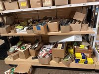 Photo of multiple cardboard boxes filled with assorted hardware items on metal shelving including planter bands, hooks, nails, and fasteners.