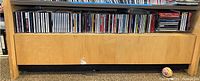 Wide view of wooden shelf filled with multiple CDs lined up in jewel cases