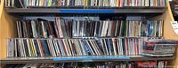 Shelf stacked with multiple rows of CD jewel cases, mostly standard sizes, covering various artists and genres.