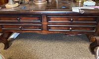 Front view of dark wood coffee table showing four drawers with round knobs and scratches on surface.