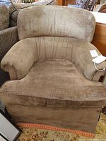 Front view of a brown velvet swivel armchair with rounded back and pleated skirt base