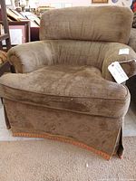 Front and angled front view of a brown fabric swivel armchair with pleated skirt and nailhead trim, showing padded backrest and armrests