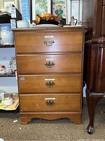 Front view of wood dresser with four drawers, brass handles, and stickers on drawer fronts.