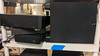 A photo showing a black Russound subwoofer R10DT and stacked black media players on a white metal shelving unit.