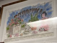 Framed Asian art print showing an Asian doll in a pink kimono sitting inside a shop window surrounded by flowers, plants, and decorative objects.