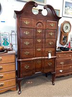 Front view of wood highboy dresser showing five drawers, carved shell decoration, brass handles, and curved cabriole legs.