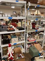 View of two assembled tall white plastic shelving units holding various household items (excluded from sale). Shelves are slatted plastic with tubular legs.