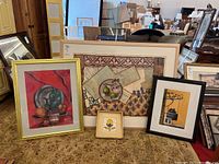 Four framed wall art pieces arranged on a table showing variety in style and frame colors.