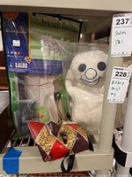 French Bulldog whirligig in packaging, Pillsbury Doughboy dog toy wrapped in plastic, and decorative mask shown together on shelf.