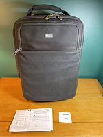 Front view of black Think Tank camera bag standing upright on table with instruction manual and lot tag displayed in front.
