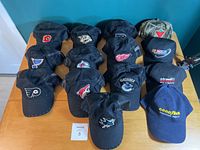 Front view of all 14 hats on wooden table, showing NHL logos and branded caps