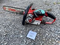 Overall view of the Homelite Super Mini chainsaw showing the full length of the chain bar and body resting on gravel.