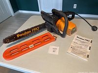 Overview photo showing Poulan Pro 300E chainsaw, orange chainsaw guard, and operator's manual on table.