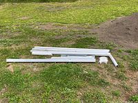 Overview of white downspout and eavestrough pieces laid on grass including straight sections and elbow pieces.