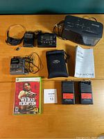 Various electronics including headphones, Sony Walkman players, Dream Machine clock radio with manual, FM transceivers, and Xbox 360 game with case and manual on table.