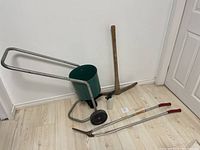 Photo showing full lot with seed spreader, pickaxe, hedge clippers, and spray bottle arranged on floor against wall.