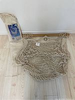 Rope hammock swing laid out on floor showing wooden spreader bar, hanging ring, and woven rope seat.