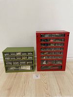 Two metal hardware organizers, red and green, with various small drawers containing assorted hardware items, viewed from front
