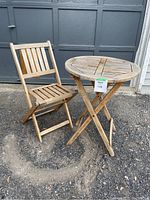 Wooden folding patio chair and round table placed outdoors on gravel and concrete.