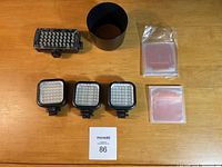 All items arranged on wooden table including Manfrotto ML360 light panel, three small Rocketfish LED lights, Canon lens hood, and color filter sets in sleeves.