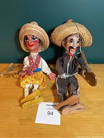 Front view of both male and female puppets seated, showing straw hats and colorful clothing with strings attached.