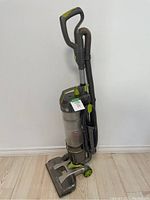 Full view of Hoover Air WindTunnel upright vacuum cleaner showing handle, hose, and base with wheels on wood floor against white wall.