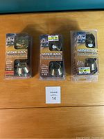Front view of three Weiser lock sets in original packaging on a wooden surface, showing brand and series label with price stickers.