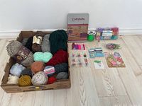 Yarn balls in a box alongside three bead kits and various jewelry making supplies laid out on the floor.