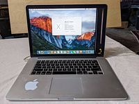 Front view of MacBook Pro with screen on, showing OS X El Capitan and minor bottom corner screen damage on right.