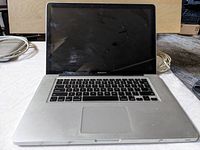 Front view of silver 15 inch MacBook Pro with cracked screen, keyboard, and trackpad, showing wear and damage on screen and body.