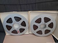 Two 10-inch metal reels loaded with brown magnetic tape, side by side on a dark fabric background.